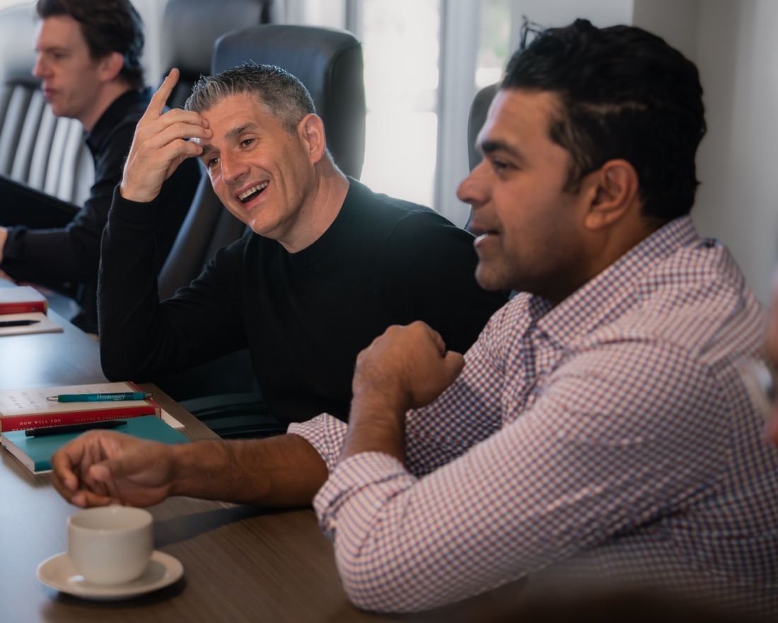 Herringbone team members laughing and talking around a conference table with coffee and notebooks