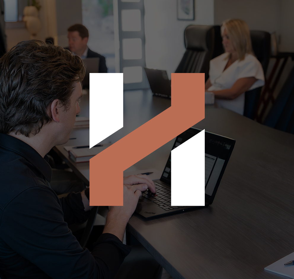 Herringbone team working on laptops around a conference table, under a dark overlay with the Herringbone H mark
