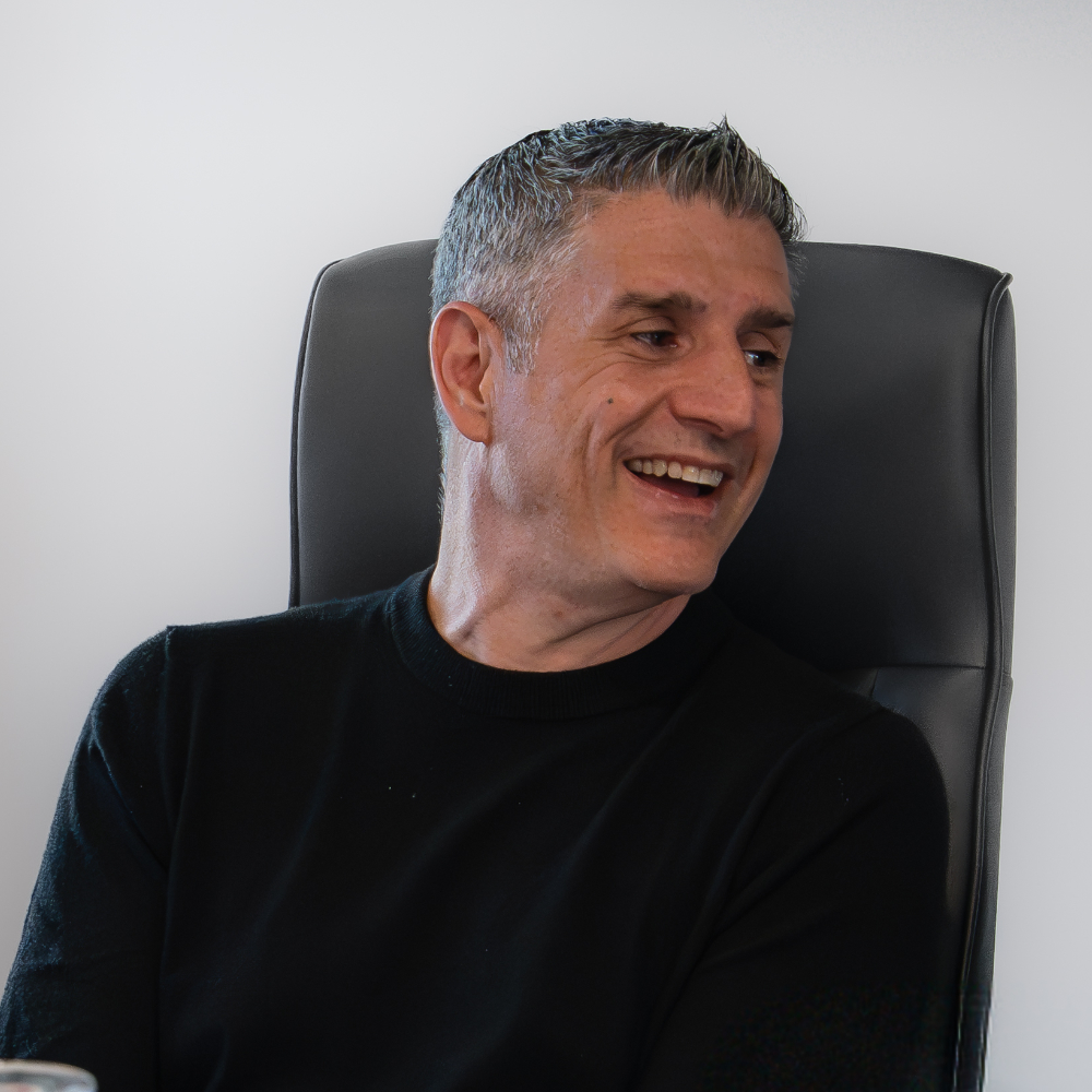A Herringbone leader in a black sweater laughing in a meeting chair
