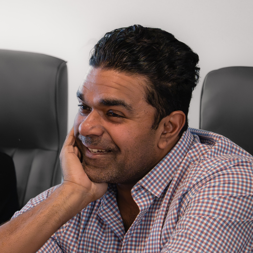 A Herringbone team member in a checked shirt smiling, his chin resting on his hand