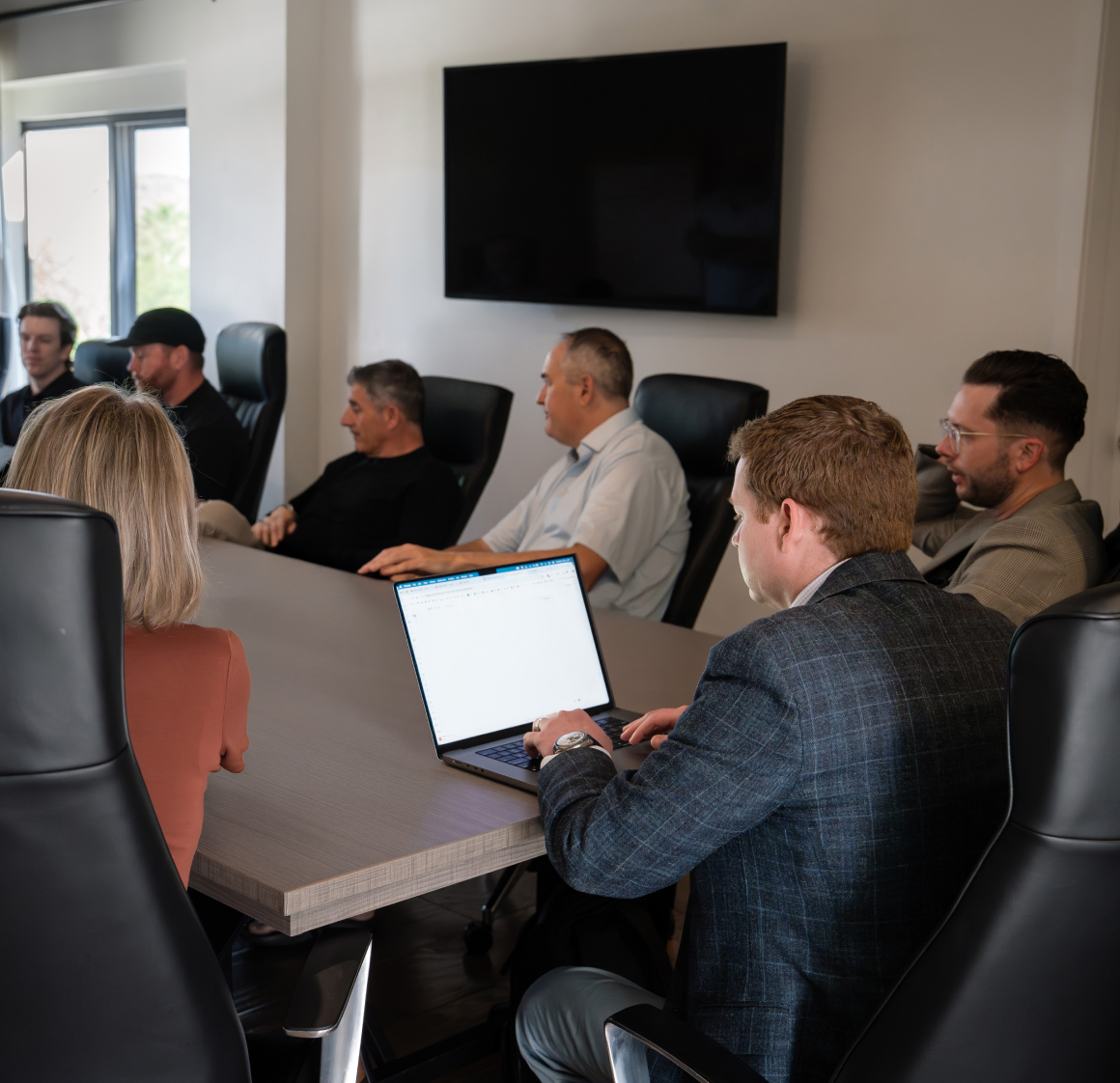 Herringbone team seated around a conference table, one colleague typing on a laptop in the foreground