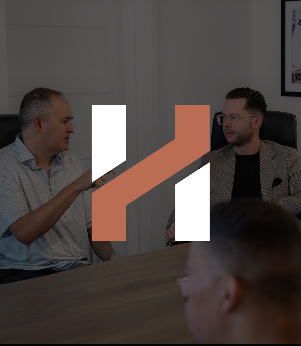 Two Herringbone colleagues talking across a conference table, under a dark overlay with the Herringbone H mark