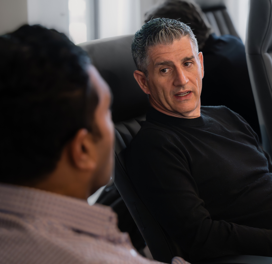 A Herringbone leader in a black sweater in conversation with a colleague in a checked shirt
